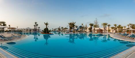 A large outdoor swimming pool with multiple lounge areas and palm trees.