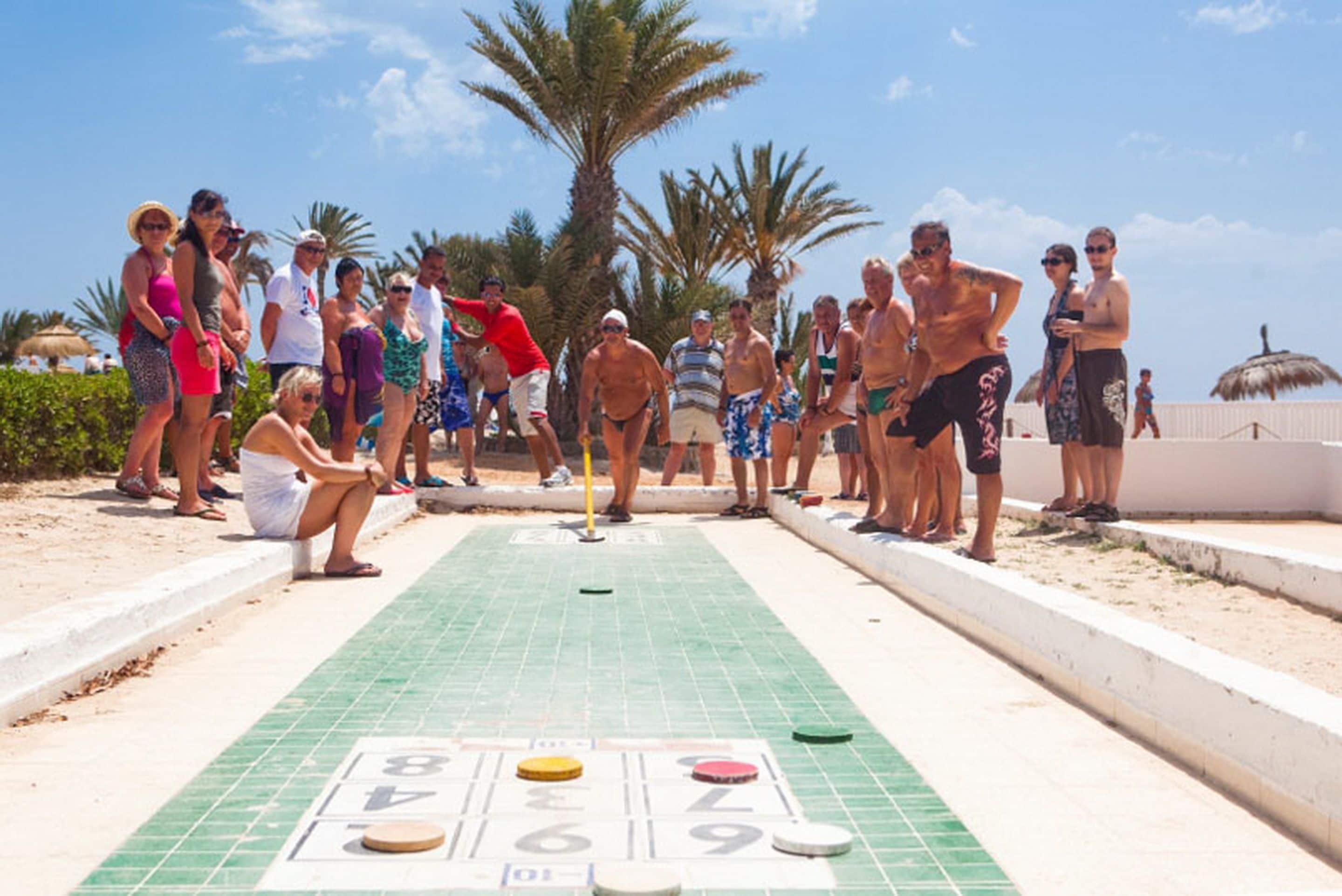 A group of people playing shuffleboard on a tiled court with numbered scoring areas.