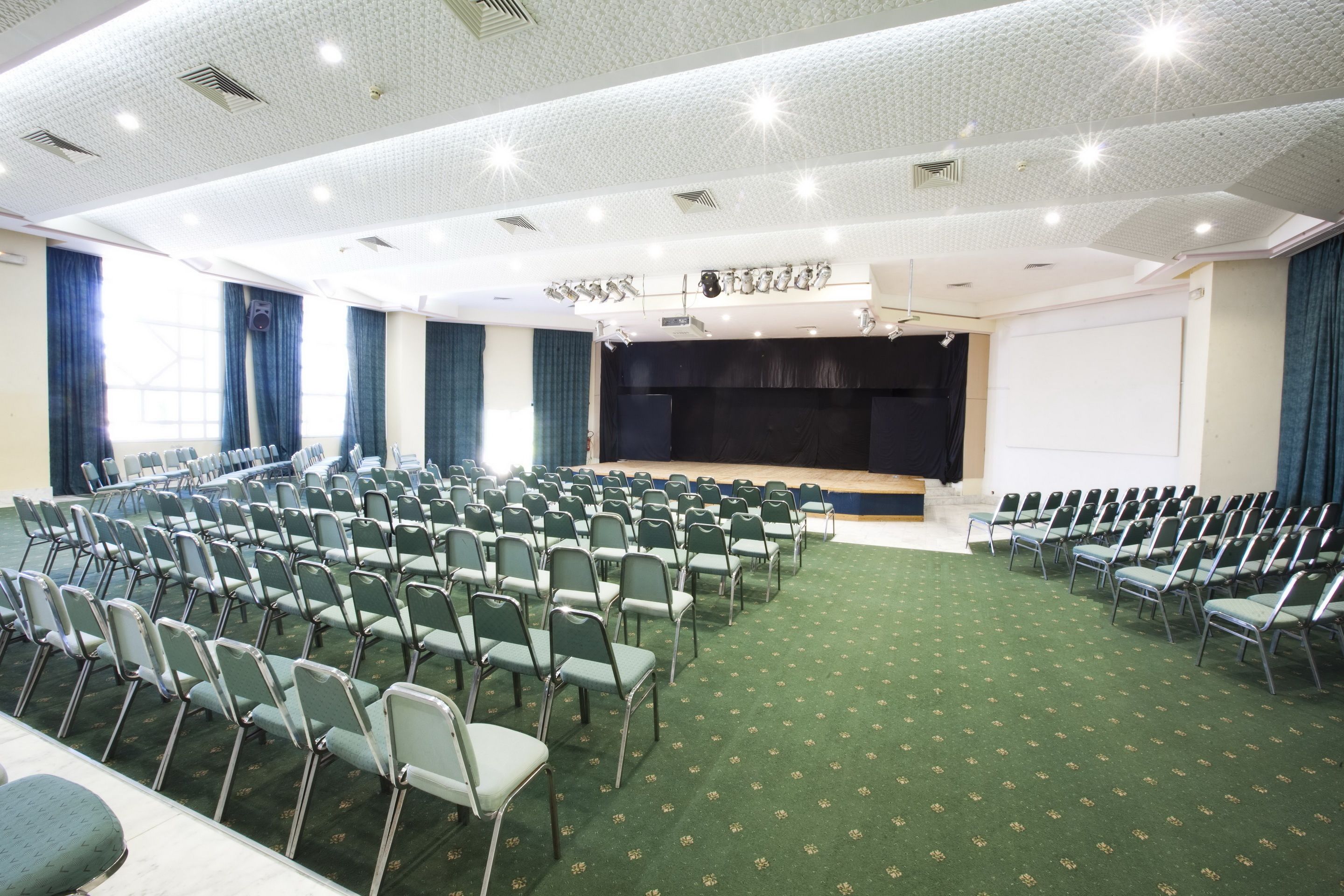 A conference room with rows of chairs, a stage, and a projector screen.