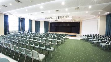 A conference room with rows of chairs, a stage, and a projector screen.