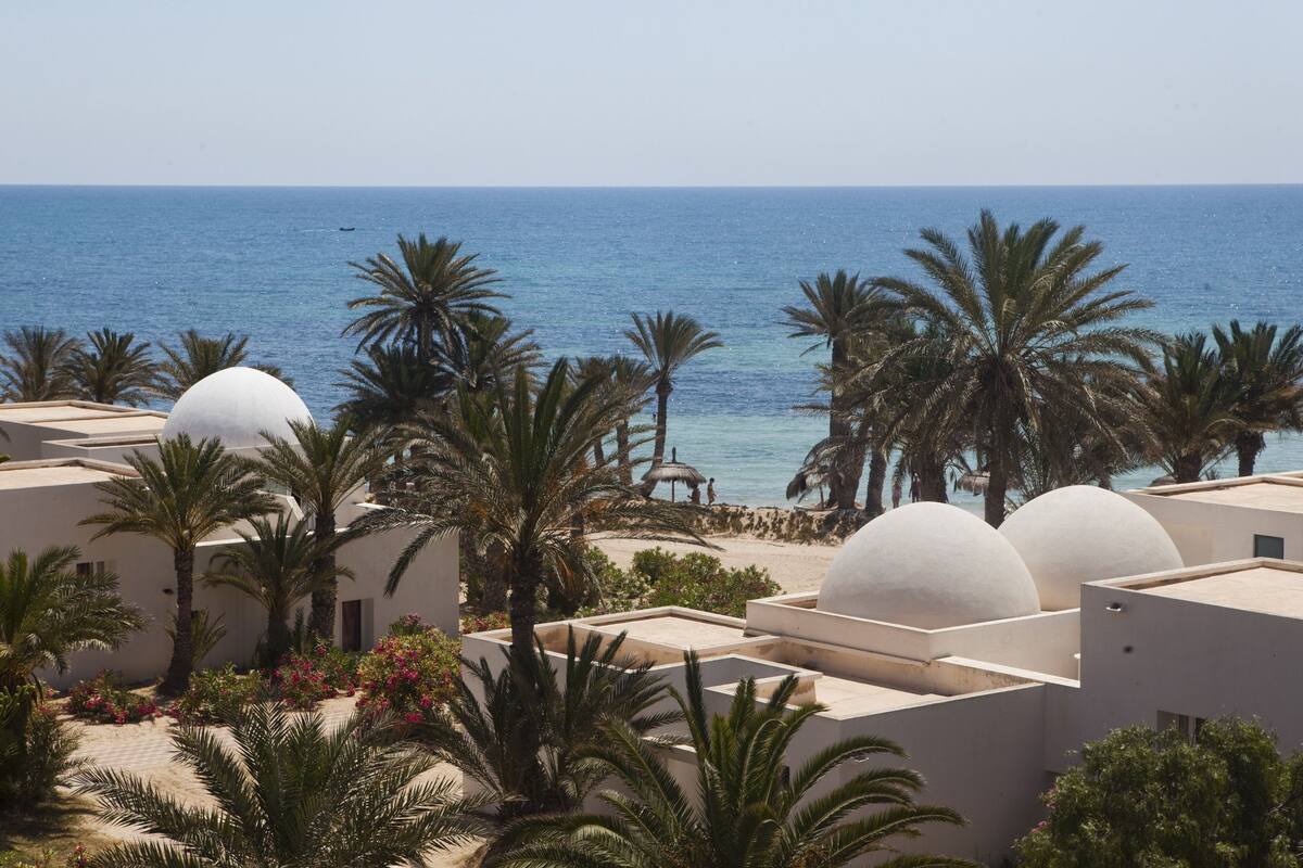 A resort with palm trees, white domed buildings, and a beach view.