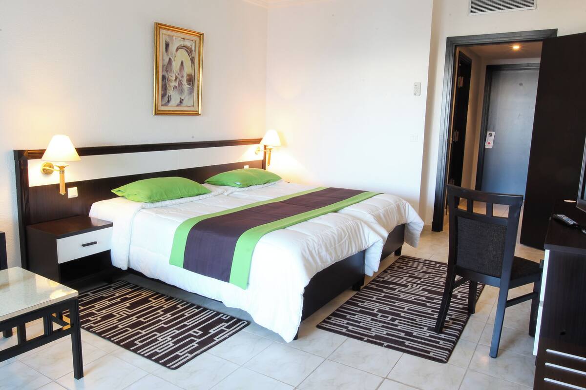 A hotel room with a bed, bedside tables, a desk, a chair, a television, and a lamp.