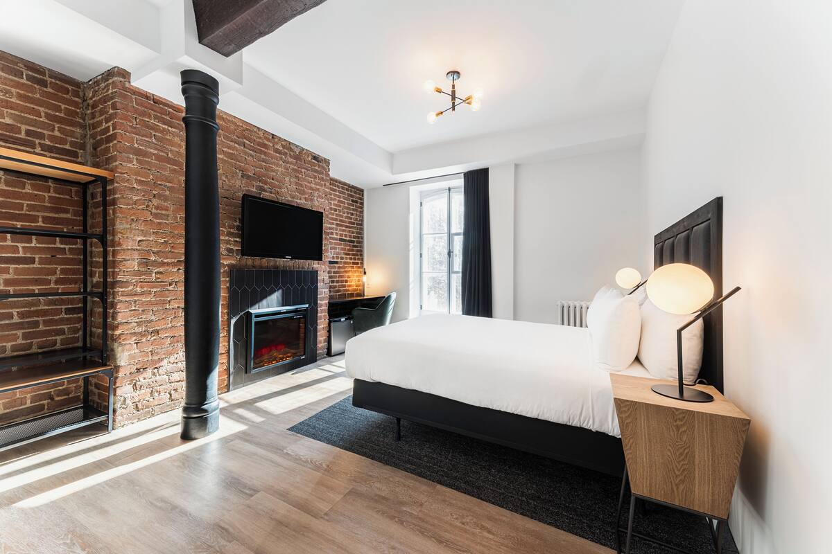 A modern bedroom with a brick fireplace, a large bed, and a wooden nightstand.