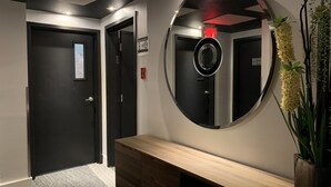 Un couloir avec un banc en bois, un miroir rond et une plante en pot.
