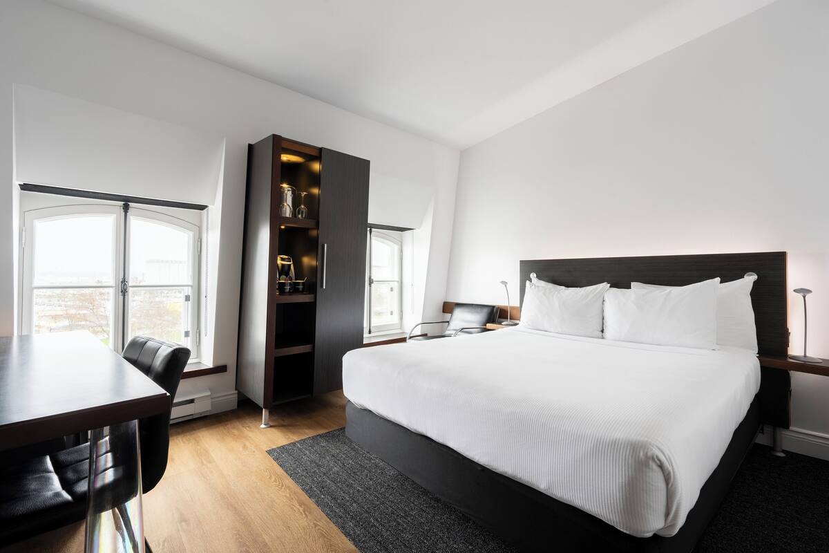 A modern hotel room with a large bed, a desk, and a built-in shelving unit.