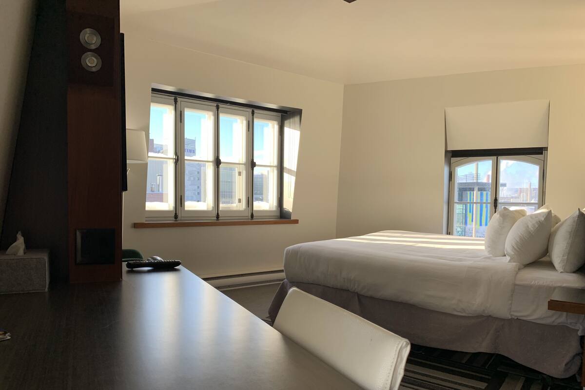 A hotel room with a large bed, a desk, and a window with a city view.