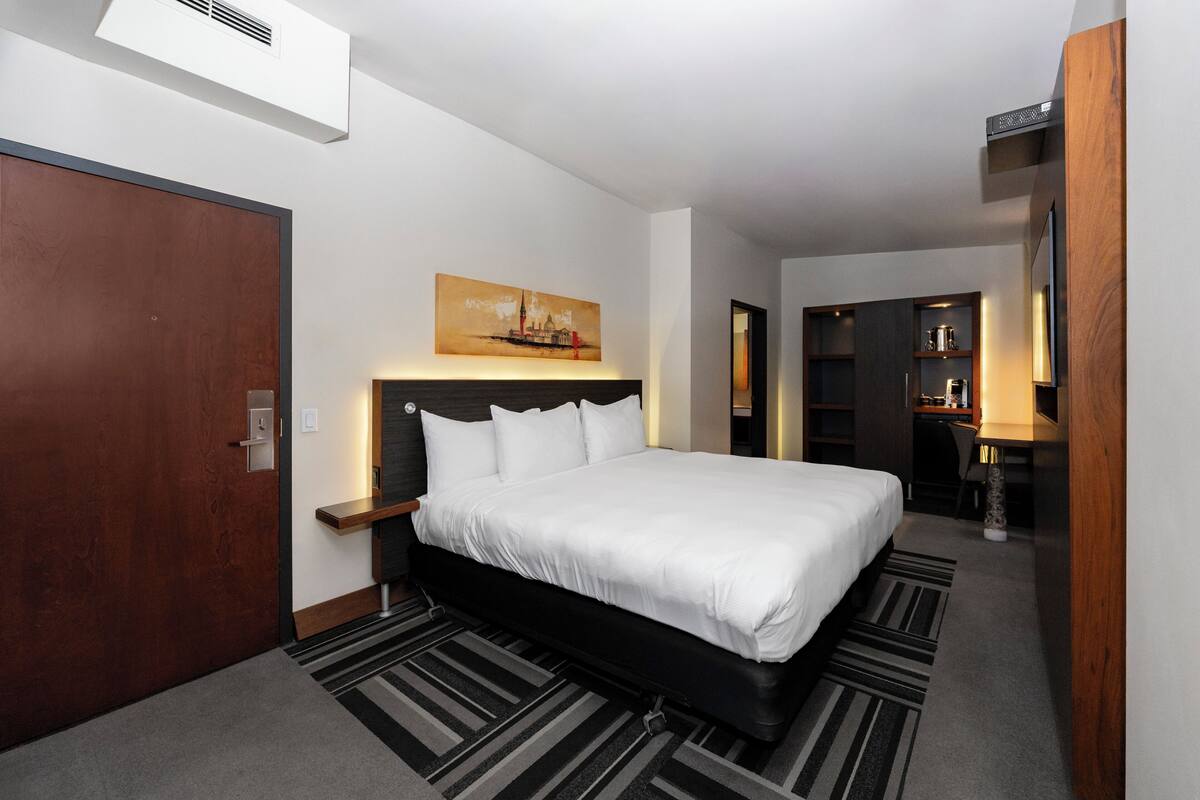 A modern hotel room with a large bed, a desk, and a bookshelf.