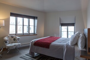 Una habitación de hotel con una cama, una silla, un ventanal y una lámpara.