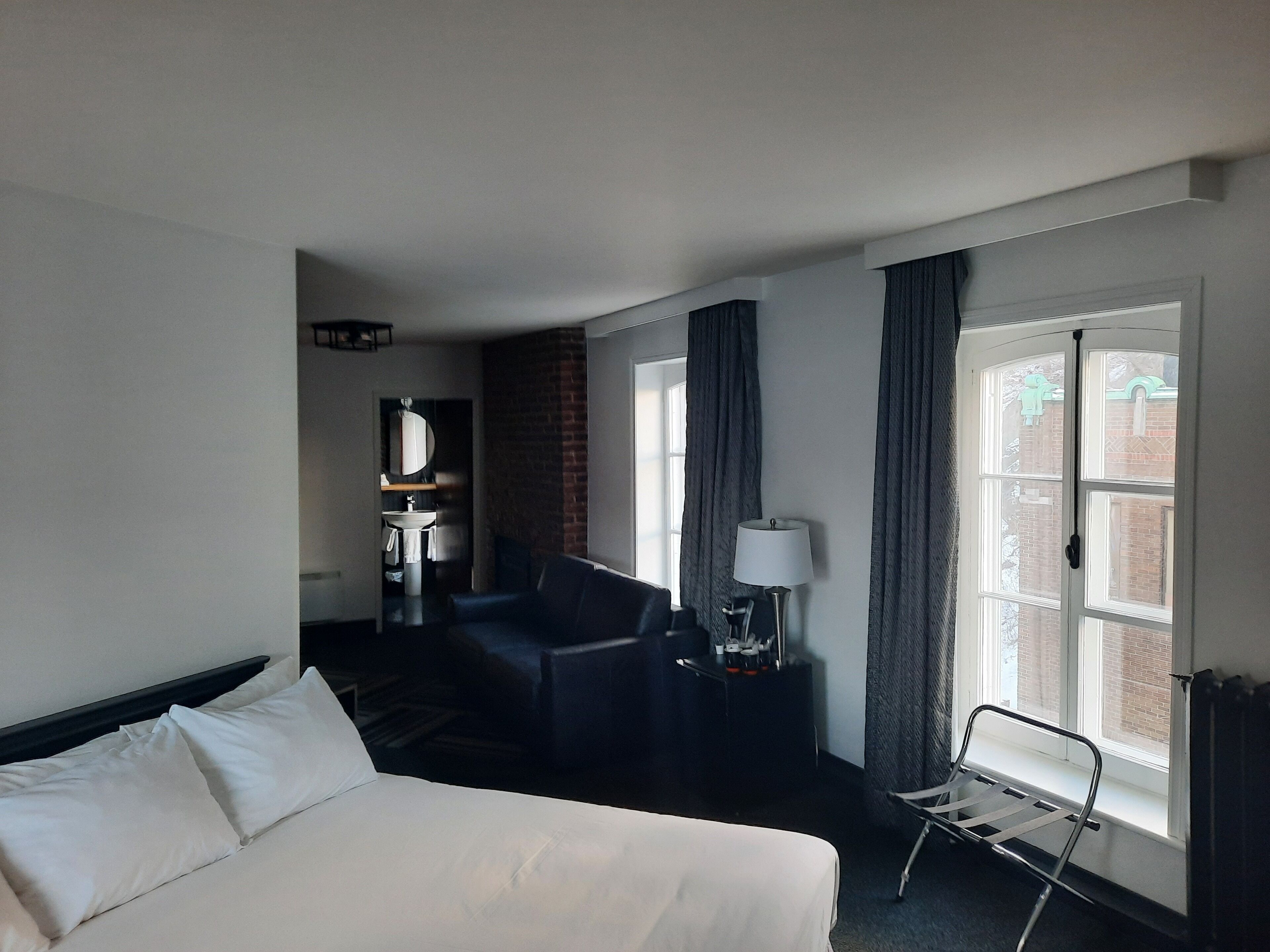 Habitación de hotel con cama, escritorio, silla, lámpara y ventana con cortinas.