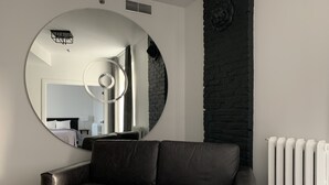 Un salon moderne avec un grand miroir rond, un canapé en cuir noir, un radiateur blanc et un mur en pierre.