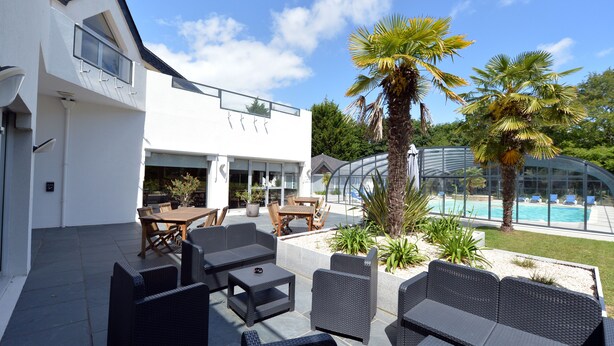 Un patio moderno al aire libre con mobiliario de mimbre, piscina y palmeras.