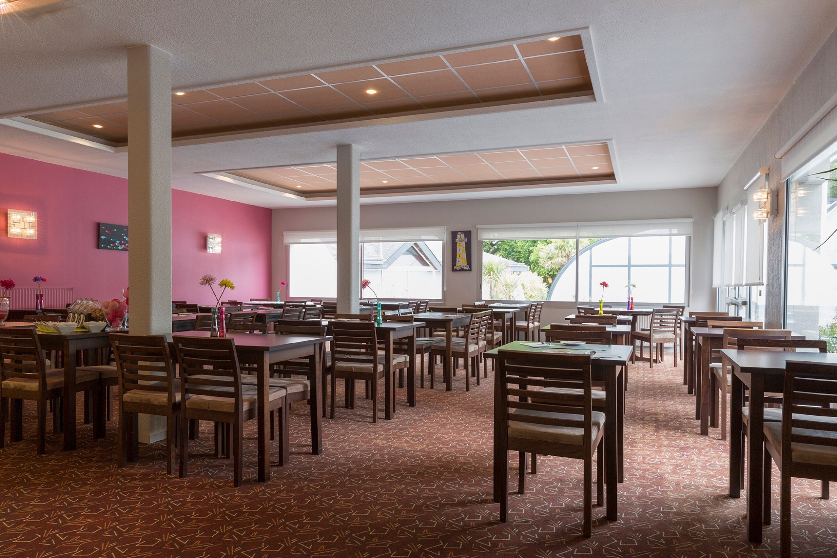 A spacious dining area with multiple tables and chairs, large windows, and a patterned carpet.