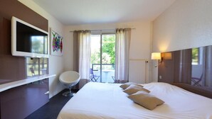 Habitación de hotel con una cama grande, un televisor montado en la pared, una silla, una mesa y vistas al exterior a través de una puerta corrediza.
