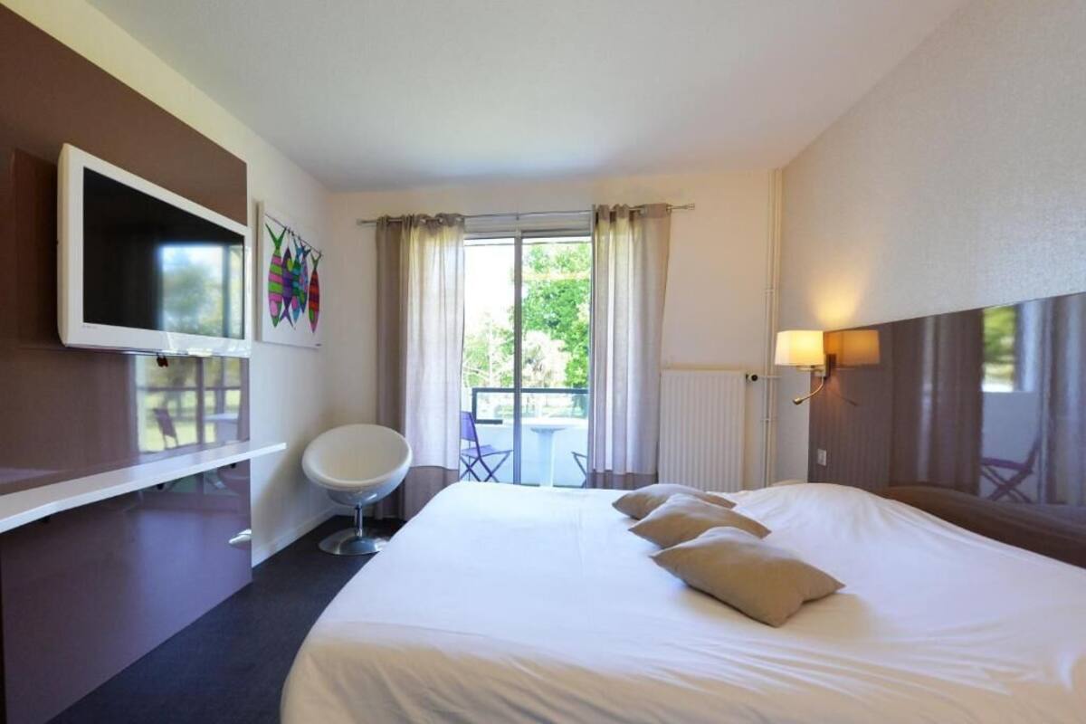 Habitación de hotel con una cama grande, un televisor montado en la pared, una silla, una mesa y vistas al exterior a través de una puerta corrediza.