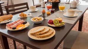 Una mesa de desayuno con cruasanes, huevos, queso, pan, fruta y bebidas.