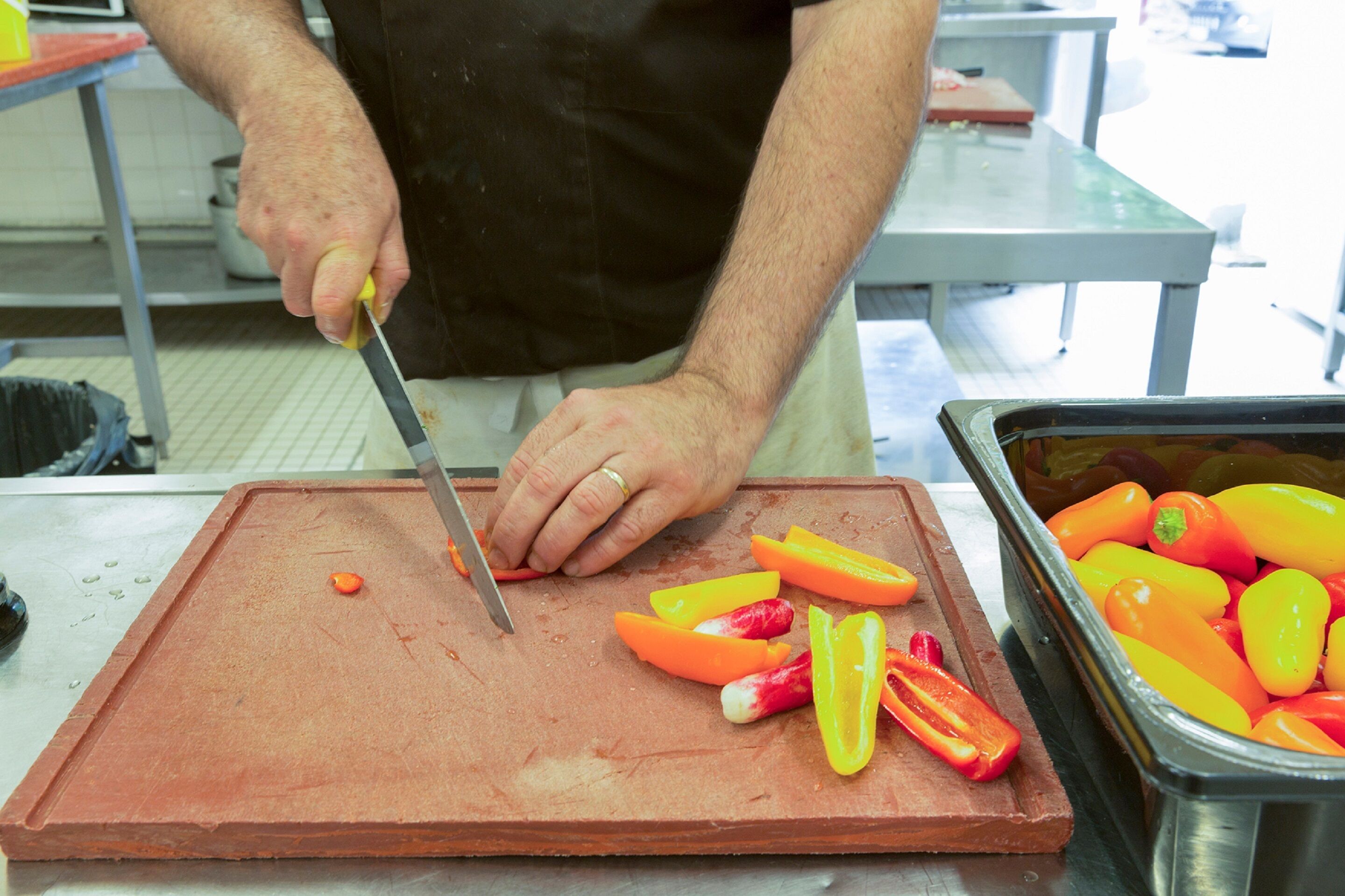 Une personne qui coupe des poivrons sur une planche à découper dans une cuisine.