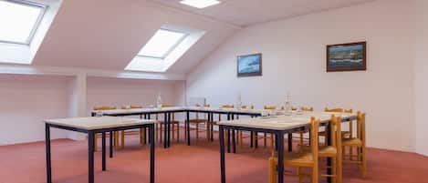 Een vergaderzaal met tafels en stoelen, dakramen en wanddecoraties in lijsten.