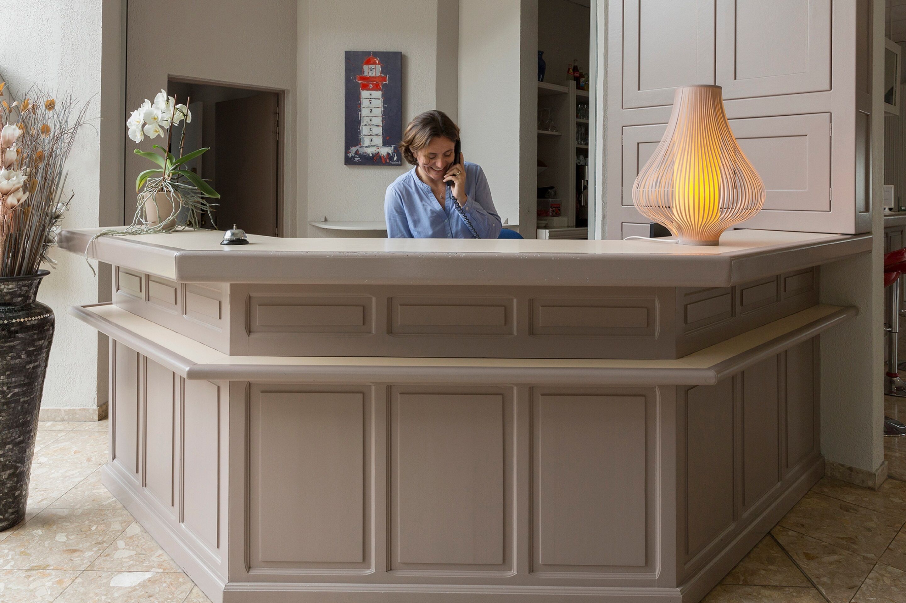 A reception desk with a vase of flowers, a painting of a lighthouse, and a lamp.
