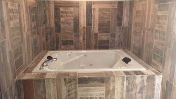 A rectangular bathtub with a single faucet and a black seat, surrounded by wooden-patterned tiles.