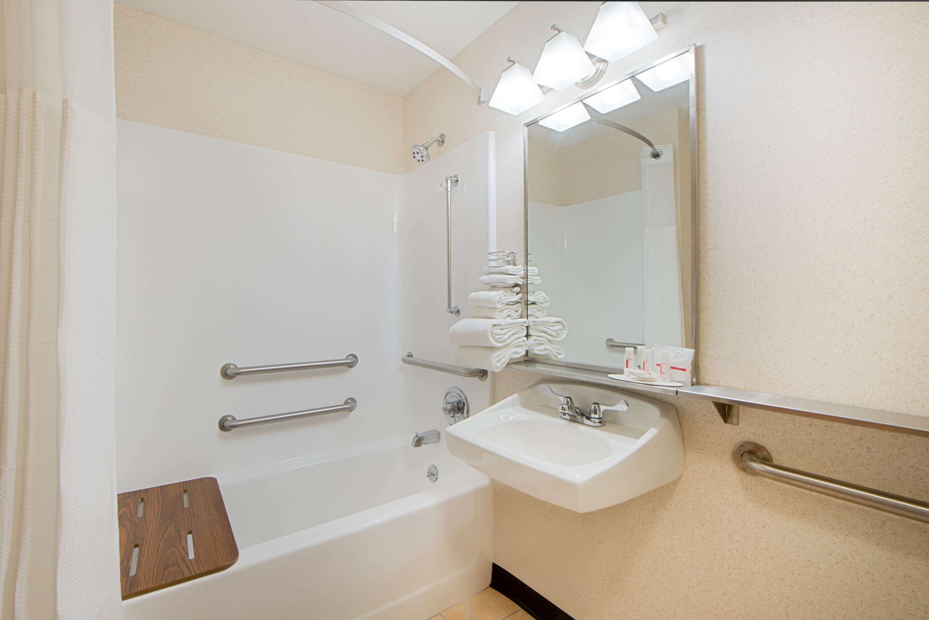 A bathroom with a bathtub, a sink, a mirror, and handrails.