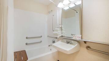 A bathroom with a bathtub, a sink, a mirror, and handrails.