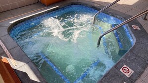 Un jacuzzi con una escalera metálica, rodeado de suelo con baldosas y un cartel que dice 'No Running'.