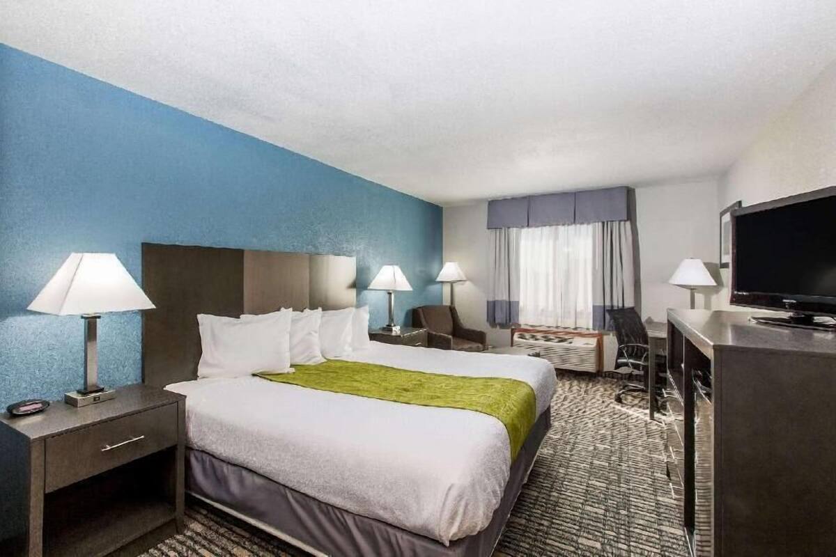 A hotel room with a bed, two bedside tables with lamps, a desk with a chair, a television, and a window with curtains.