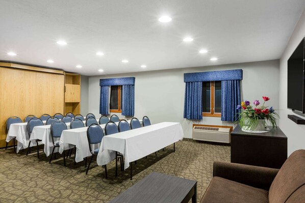 Un salón de conferencias con mesas, sillas, una pantalla grande y un arreglo floral.