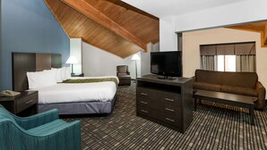 Una habitación de hotel con una cama grande, un escritorio con televisor, un sofá y una silla.