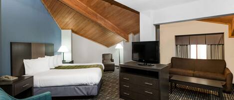 A hotel room with a large bed, a desk with a TV, a sofa, and a chair.