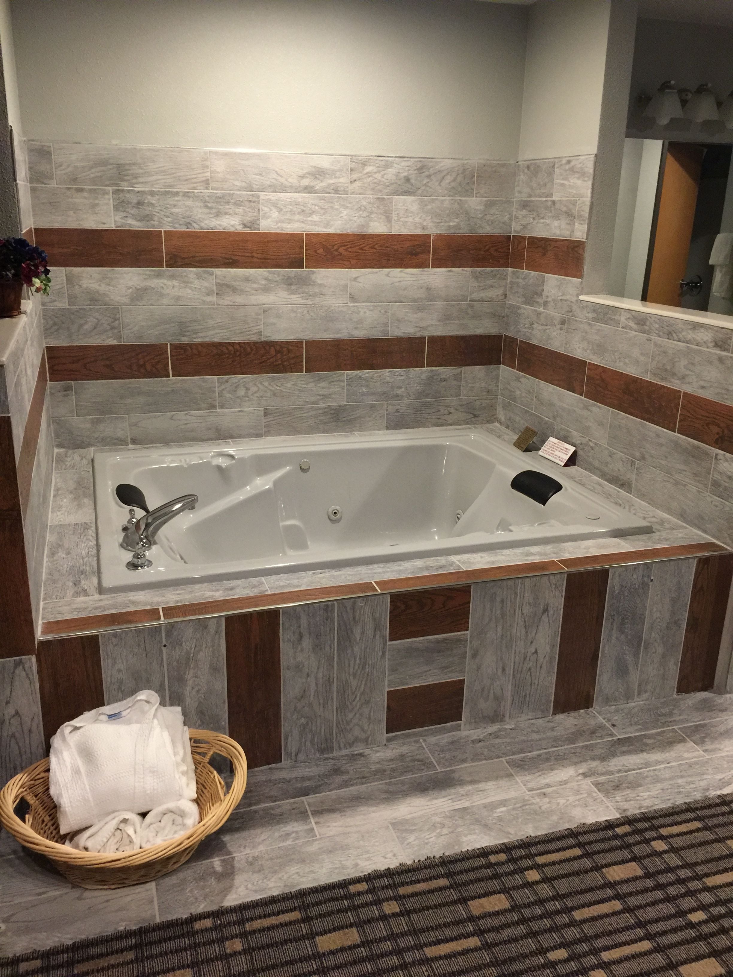 A modern bathroom with a freestanding bathtub, wooden and stone tile walls, a wicker basket with towels, and a patterned rug.