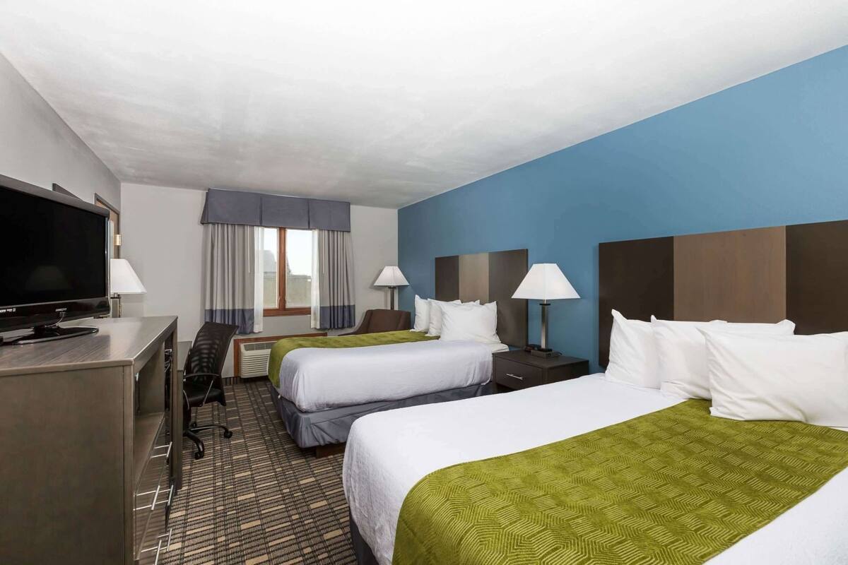 A hotel room with two beds, a desk with a TV, a chair, and a window with curtains.