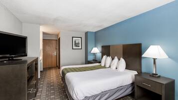 Una habitación de hotel con cama, mesitas de noche, televisor y alfombra estampada.