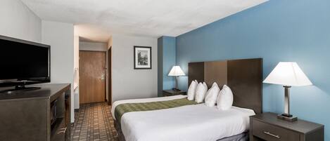 Una habitación de hotel con cama, mesitas de noche, televisor y alfombra estampada.
