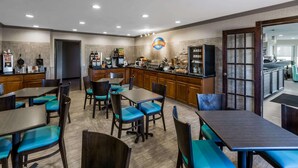 Un comedor de hotel con mesas y sillas, una estación de café y vistas hacia la cocina.