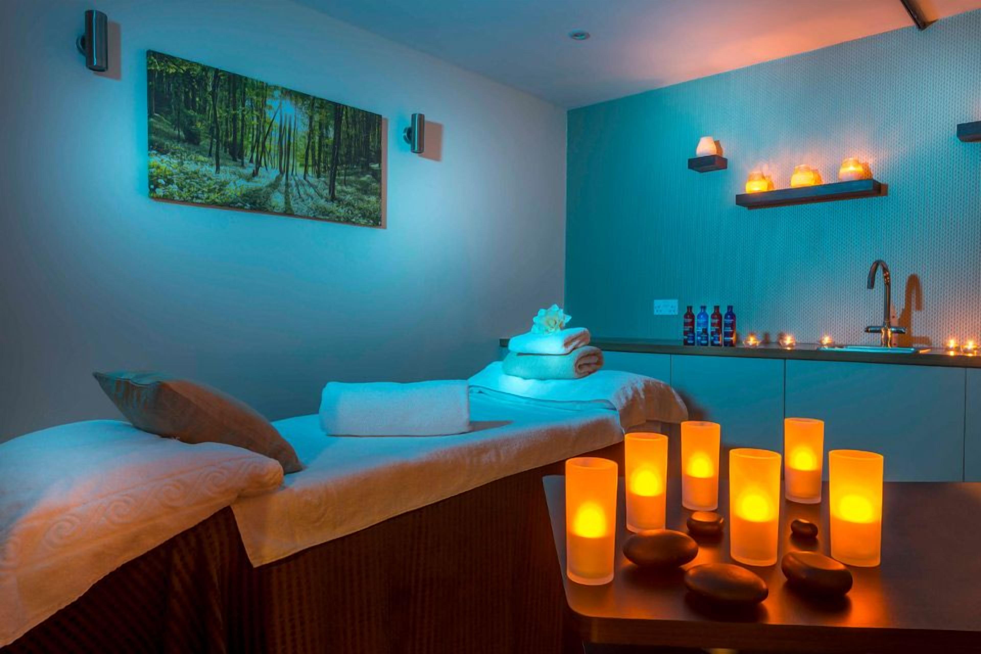 A spa room with a massage table, candles, and a painting on the wall.