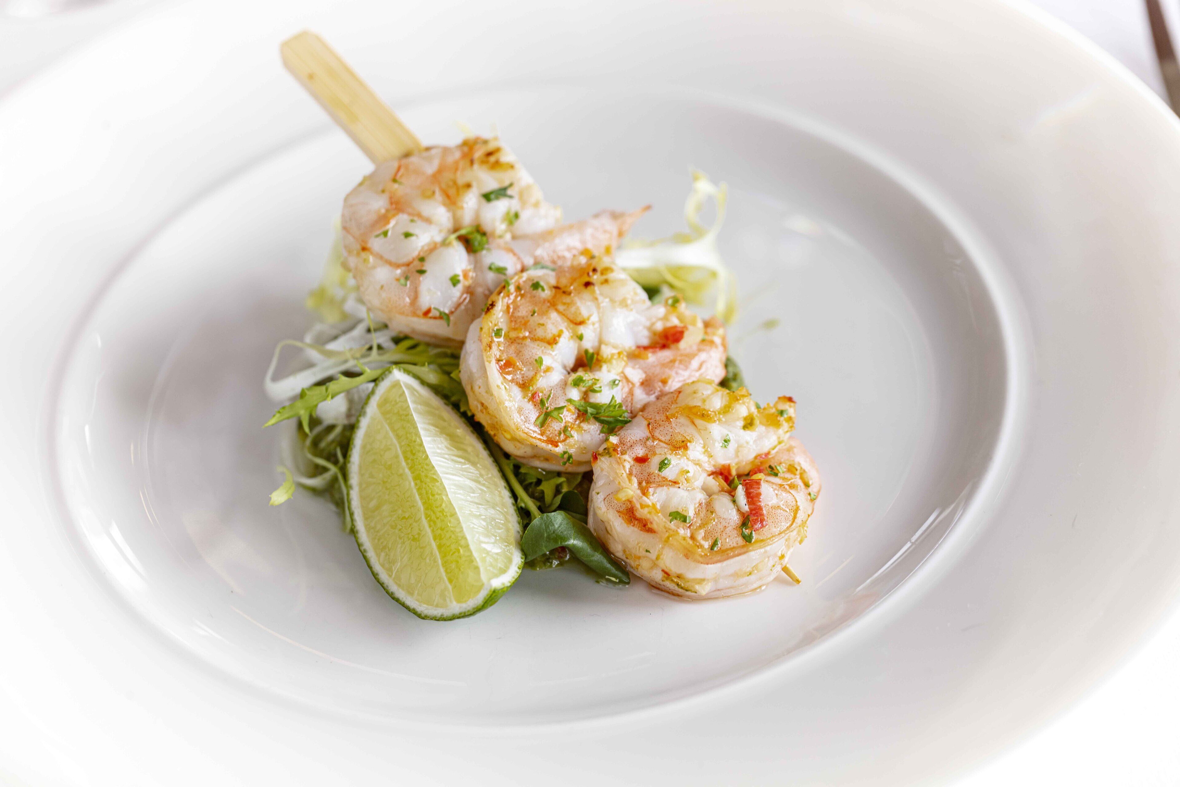 A plate of shrimp on a bed of greens and a lime wedge.