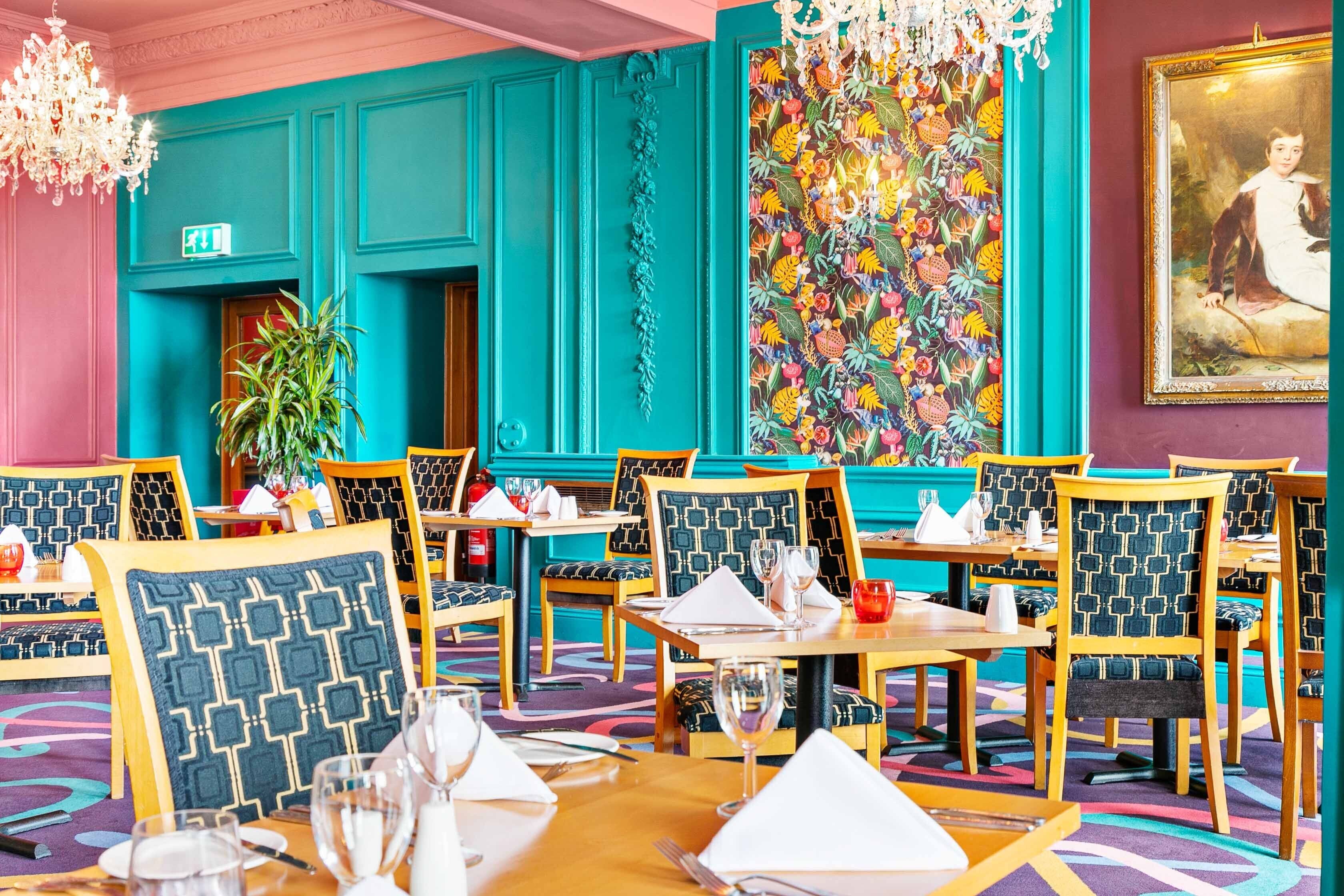 A restaurant with teal walls, patterned chairs, and a colorful floral wall decoration.