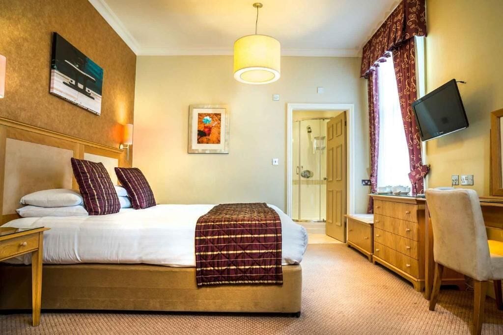 A hotel room with a bed, a desk, a chair, a television, and a door leading to a bathroom.