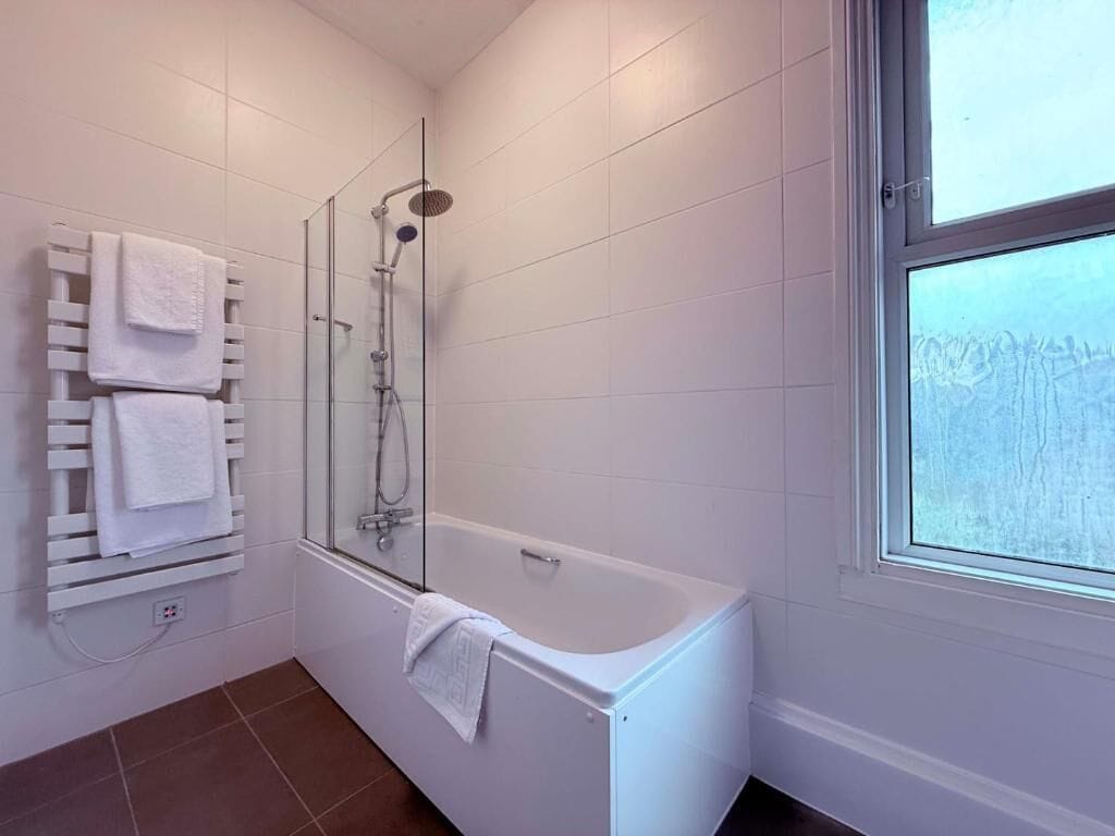 A modern bathroom with a glass-enclosed shower, a white bathtub, and a towel rack with multiple towels.