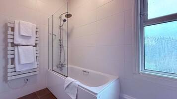 A modern bathroom with a glass-enclosed shower, a white bathtub, and a towel rack with multiple towels.