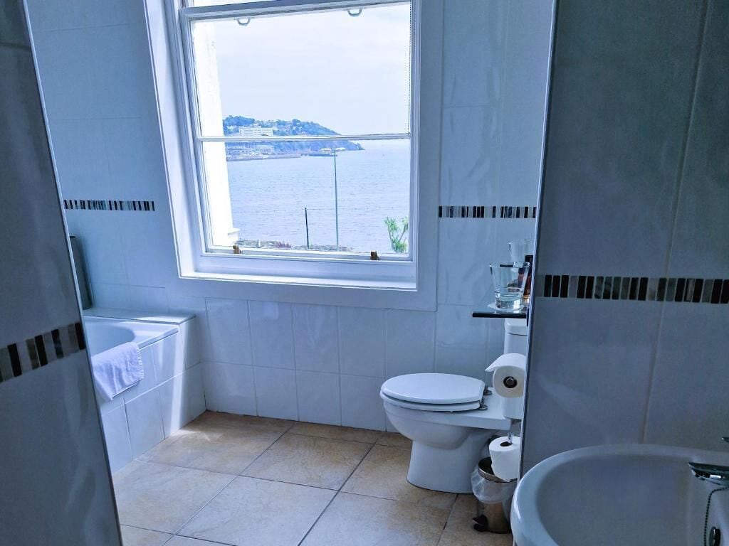 Une salle de bain équipée de toilettes, d’un lavabo et d’une fenêtre donnant sur un plan d’eau.