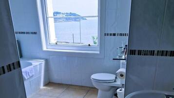 Une salle de bain équipée de toilettes, d’un lavabo et d’une fenêtre donnant sur un plan d’eau.