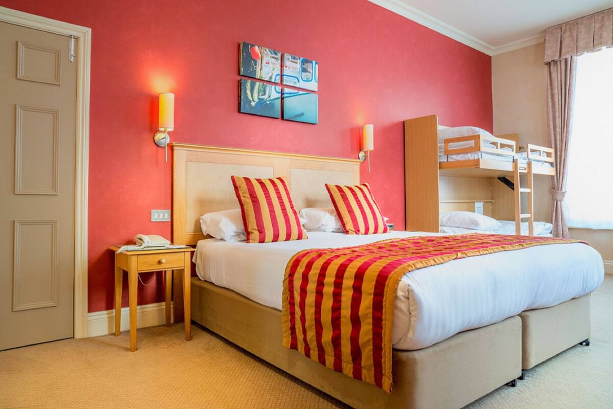 Ein Hotelzimmer mit einem Bett, einem Nachttisch, einer Lampe, einem Stockbett und einem Gemälde an der Wand.