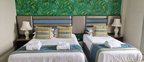 A hotel room with two beds, each with a headboard, bedside tables, lamps, and towels.