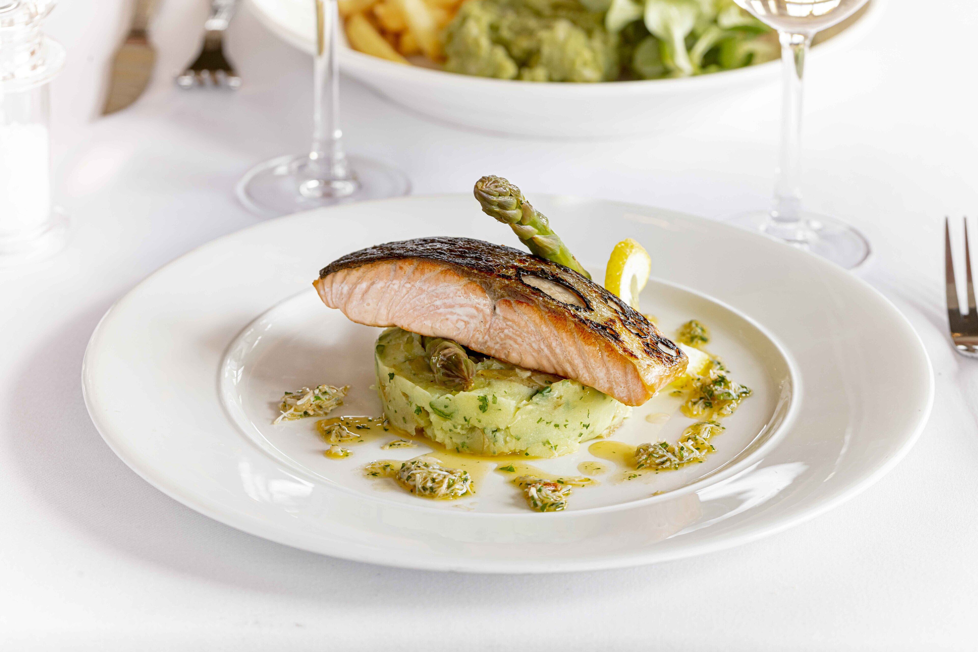A plate of food with a piece of grilled fish, asparagus, and a lemon wedge on top, served on a white plate.