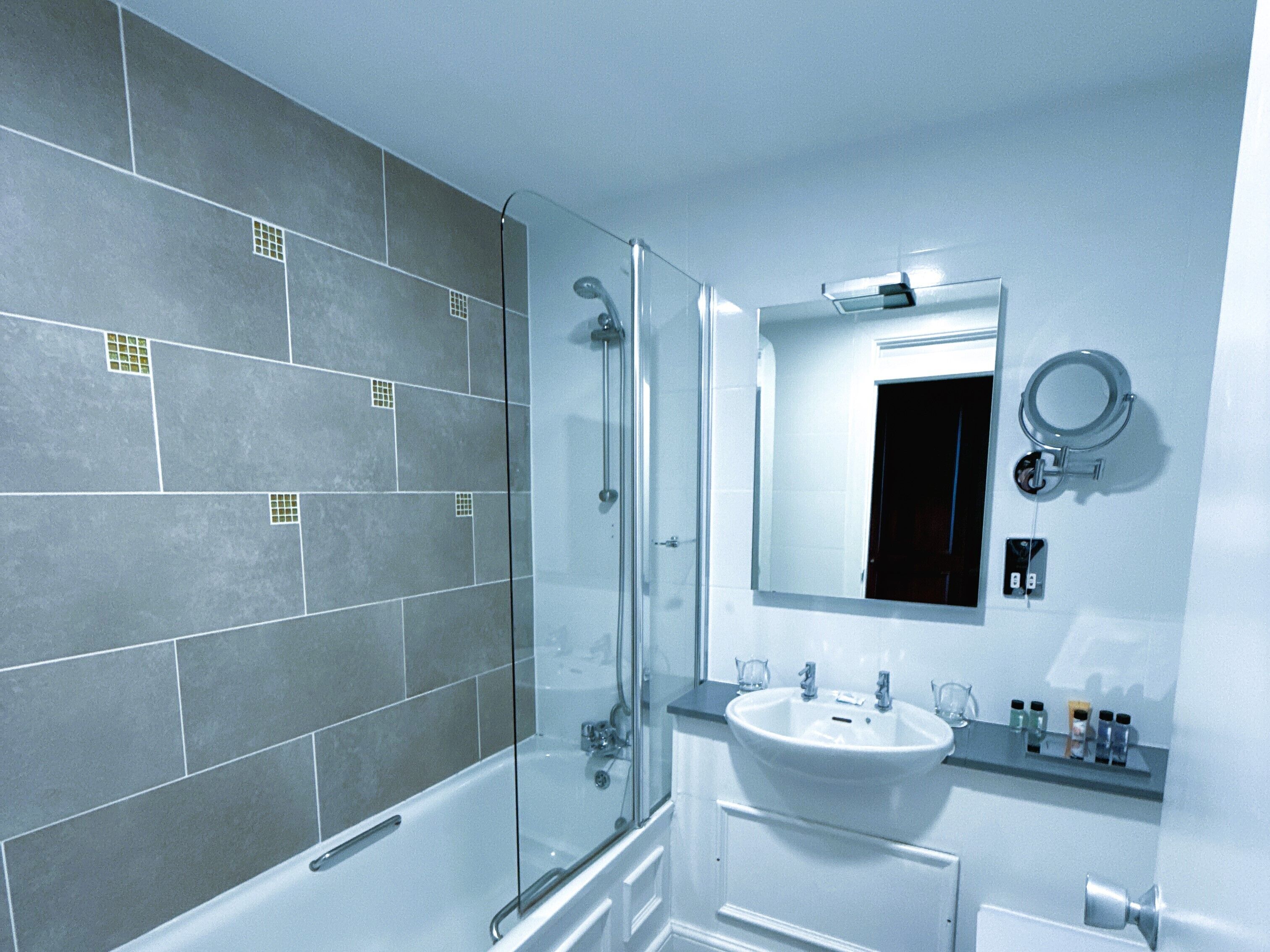 Un baño moderno con ducha envuelta en vidrio, lavamanos blanco y espejo sobre él.