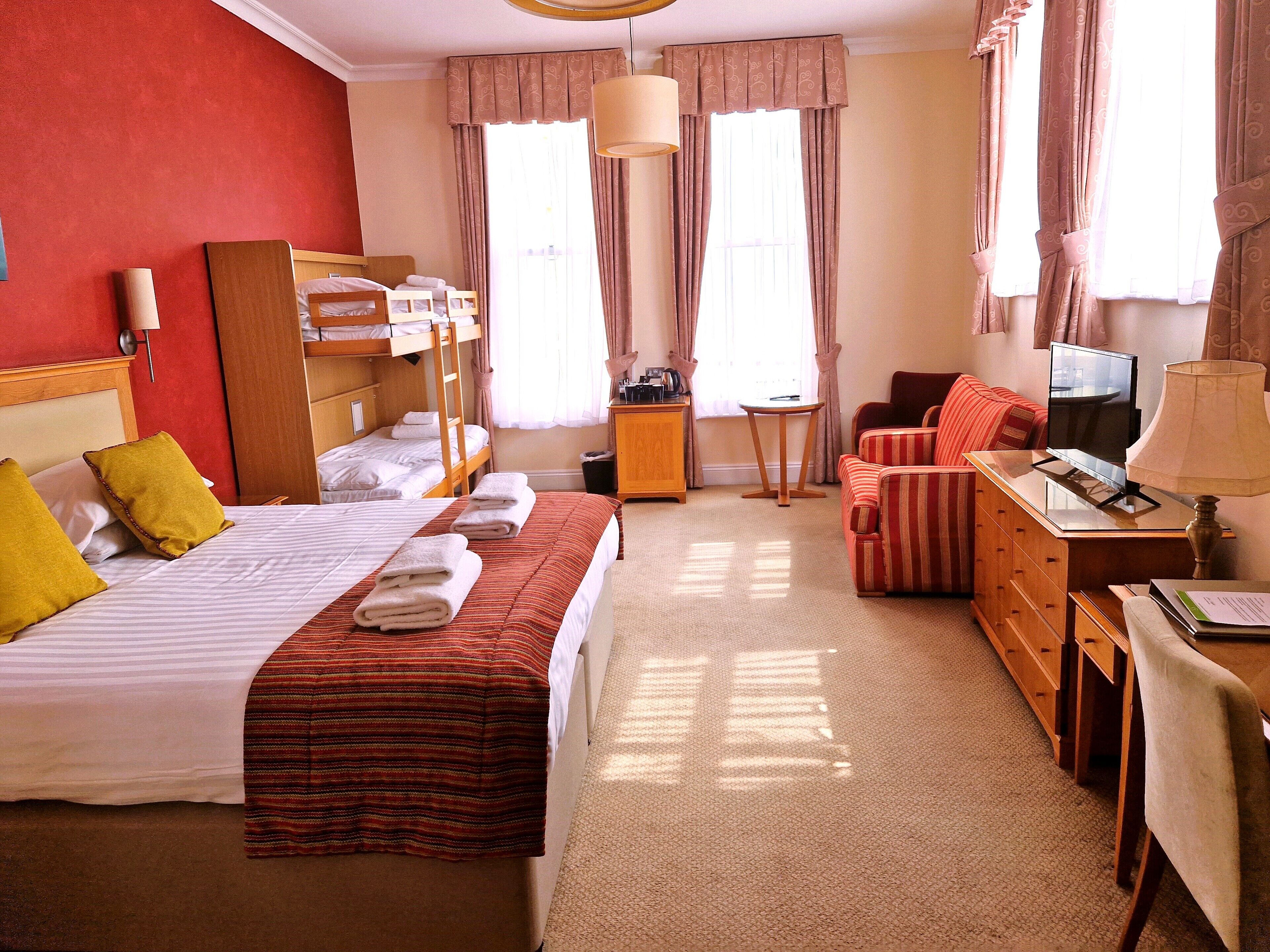 A hotel room with a bed, a desk, a chair, a TV, and a lamp.
