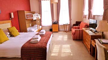 A hotel room with a bed, a desk, a chair, a TV, and a lamp.