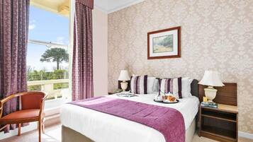 A hotel room with a large bed, a chair, a nightstand, and a window with curtains.